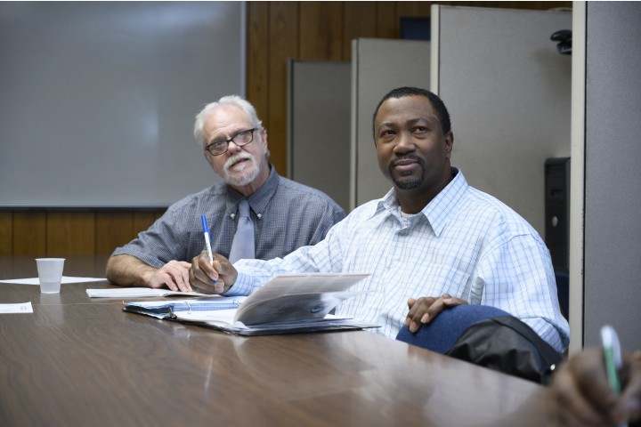 two persons sitting at a conference room table.