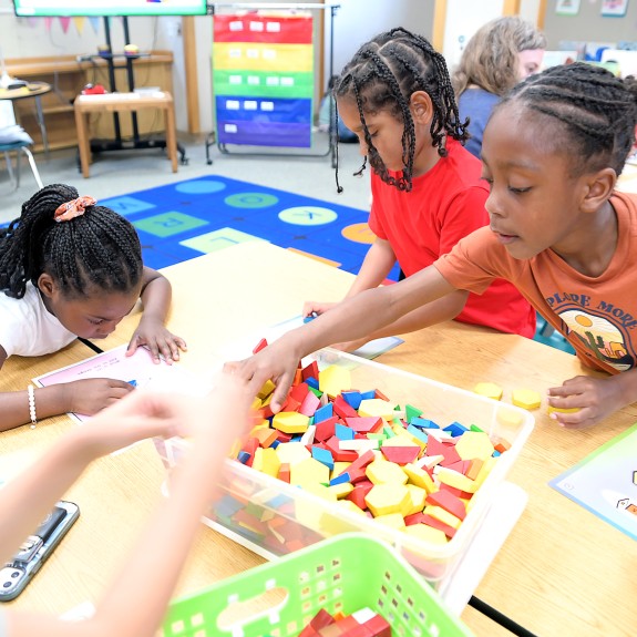 children sitting at a classroom desk reaching for toy learning blocks